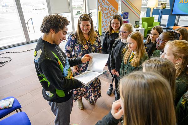 Man stands in front of group of adults and children looking at book and smiling